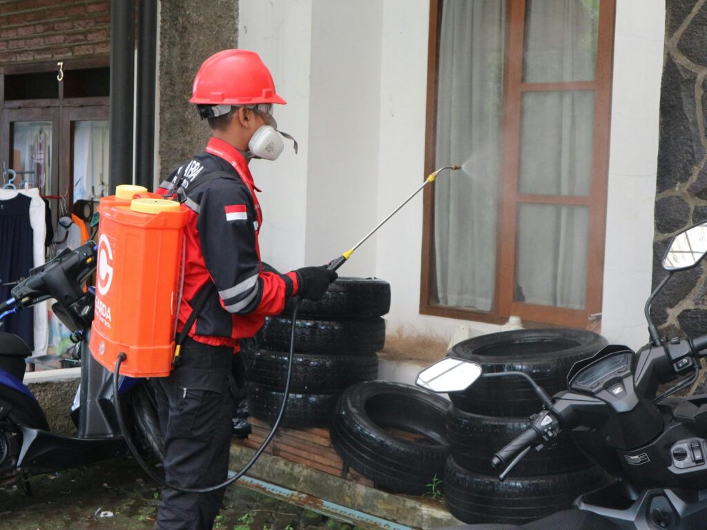 A worker in safety gear sprays disinfectant outside a building, ensuring cleanliness.
